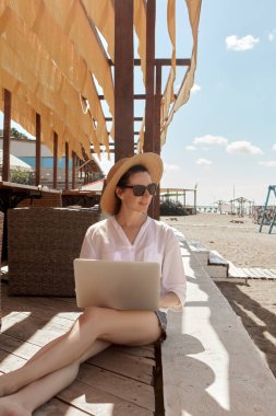 Kumsalda dizüstü bilgisayar kullanan genç bir kadın. Serbest çalışma kavramı