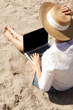 Kumsalda dizüstü bilgisayar kullanan genç bir kadın. Tatil yaşam tarzı iletişimi. Serbest çalışma kavramı