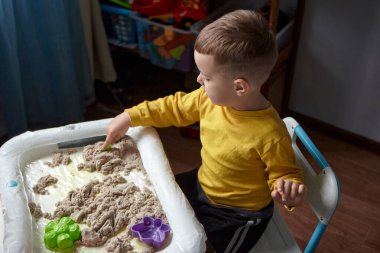 Oğlan odasında oyun oynuyor. Eğitici bir oyun. Bir çocuk karantinada kinetik kum oynar. Çocuklarda iyi motor becerilerin gelişimi