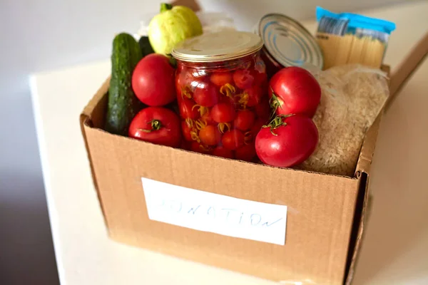 Box for a charity donation with food. Canned food, pasta, pickled tomatoes, vegetable, rice. Food delivery or food donation concept.