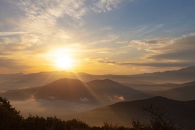 Gün doğumunda gökyüzüne karşı dağların manzarası. Dağların üzerinde görkemli bir gün doğumu