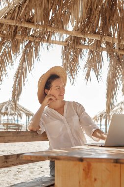 Kumsalda dizüstü bilgisayar kullanan genç bir kadın. Serbest çalışma kavramı