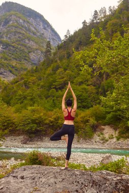 Doğada yoga dersleri. Tek başına spor yapma kavramı. Sosyal dışlama. Bir kadın kayalıklarda yoga yapıyor, bir dağ nehrinin yanında.