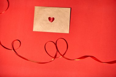 Kırmızı bir kalp Sevgililer Günü için kahverengi bir zarfın üzerinde yatıyor. Kırmızı zemin, zarf ve kırmızı kalp. Aşk mektubu ya da mesaj konsepti. Düz yatış, üst manzara. Metnin için boşluk kopyala. 