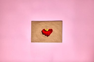 Kırmızı bir kalp Sevgililer Günü için kahverengi bir zarfın üzerinde yatıyor. Zarflı pembe zemin ve kırmızı kalp. Aşk mektubu ya da mesaj konsepti. Düz yatış, üst manzara. Metnin için boşluk kopyala. 