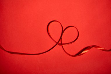 Kırmızı arka planda kırmızı kurdeleden yapılmış kalp, üst manzara. Şenlik dekorasyonu. Kalp şeklinde kurdele. Sevgililer Günü tebrik kartı.