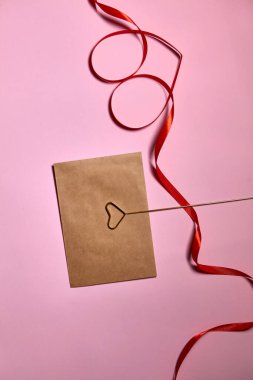 Pembe arka planda kırmızı kurdeleden yapılmış kalp, üst manzara. Şenlik dekorasyonu. Kalp şeklinde kurdele. Sevgililer Günü tebrik kartı.