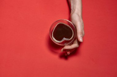 Sevgililer günü kalp geçmişi. Elinde bir fincan sıcak kahve tutan, kalp şeklinde bir fotoğraf olan bir kadın. Kırmızı arka planda şekillendirilmiş güzel dekoratif kalp, Sevgililer Günü konsepti
