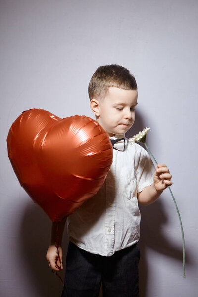 Valentine's day. Happy boy stands and holds red ball hearts on a white background. 