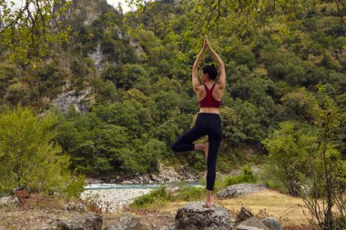 Doğada yoga dersleri. Tek başına spor yapma kavramı. Sosyal dışlama. Bir kadın kayalıklarda yoga yapıyor, bir dağ nehrinin yanında.