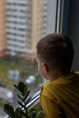 Küçük bir çocuk ne yazık ki pencereden dışarı bakıyor. Yağmurlu hava kavramı. Yağmur yüzünden çocuk evde kalıyor.