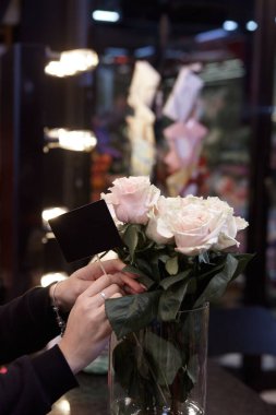 Çiçekçi renklerle çalışır. Çiçekçi, güllerin fiyatı için boş bir tabela tutuyor. Çiçekçi dükkanında maske takmış vazodaki çiçekleri kontrol ediyor..