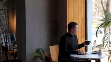 Bir kadın kafede oturuyor ve tablette çalışıyor..