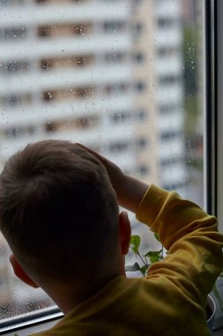 Küçük bir çocuk ne yazık ki pencereden dışarı bakıyor. Yağmurlu hava kavramı. Yağmur yüzünden çocuk evde kalıyor.