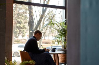 Kısa saçlı ve burun piercingli genç bir kız bir kafede oturuyor ve tablette çalışıyor. Serbest çalışma ve uzak çalışma kavramı..