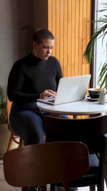 Bir kadın kafede oturur ve dizüstü bilgisayarda çalışır..