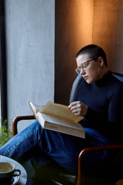 Genç bir kız bir kafede oturmuş kitap okuyor. Eğitim ve uzak çalışma kavramı 