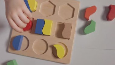 Beyaz Masa 'da oturan ve evde tahta ayırıcı ile oynayan bir çocuk. Beyaz tişörtlü bir çocuk eğitici oyunlar oynuyor. Mantığın gelişimi, şekiller ve renkler üzerine çalışma. Yüksek kaliteli FullHD görüntüler
