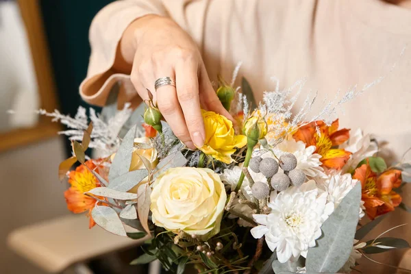 Florist works with colors. Flower seller chooses flowers for future bouquet. Flowers shop worker in a mask standing in flower shop and checking flowers in glass vase.