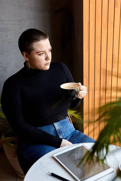 短い髪と鼻ピアスの若い女の子は カフェに座って タブレットで動作します フリーランスとリモートワークの概念 — ストック写真