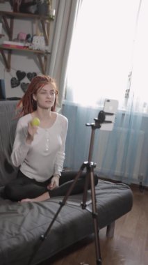 Kırmızı rastalı bir kadın blogcu video kaydediyor ya da evde akıllı telefon ve tripodla canlı yayın yapıyor. Bir kızın elinde, küçük bir top, kendine masaj eğitimi..