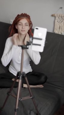 Evinde akıllı telefon ve tripodu kullanarak video kaydeden veya canlı yayın yapan bir kadın blogcu. Canlı yayın yapan canlı yayın sunucusu, dijital sosyal medya kaydediyor.