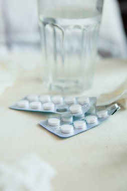 İlaçların yakın plan çekimi. Hastanın yatağının önünde mendiller, haplar, burun damlaları var. Soğuk algınlığı tedavisi konsepti.