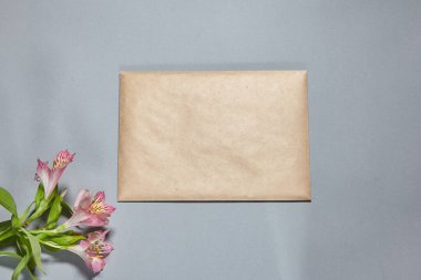 Alstroemeria çiçekleri ve gri arka planda kahverengi el işi zarfları. Kapalı el işi zarf, gri masanın üzerinde bir dal. Düz konum, üst görünüm, kopyalama alanı, alaycı