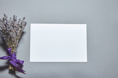 Beyaz kağıt kaplamalı lavanta çiçekleri gri arka planda. Beyaz kağıt boş, gri masada kurumuş çiçekler. Davetiye kartı mockup.Düz konum, üst görünüm, kopyalama alanı, maket