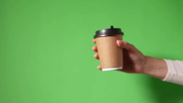 手は黒の蓋で2つのカップ茶色の紙を保持 2つのコーヒー特別オファーまたはプロモーション 女性の手は緑の画面の背景に2つのカップを保持 紅茶やコーヒーを移動します 黒蓋の茶色い紙コップ — ストック動画