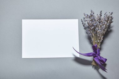 Beyaz kağıt kaplamalı lavanta çiçekleri gri arka planda. Beyaz kağıt boş, gri masada kurumuş çiçekler. Davetiye kartı mockup.Düz konum, üst görünüm, kopyalama alanı, maket