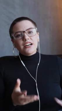 Kulaklıklı, kısa saçlı ve burun piercingli bir kızın yakın plan portresi bir kafede oturup video bağlantısıyla konuşuyor. 