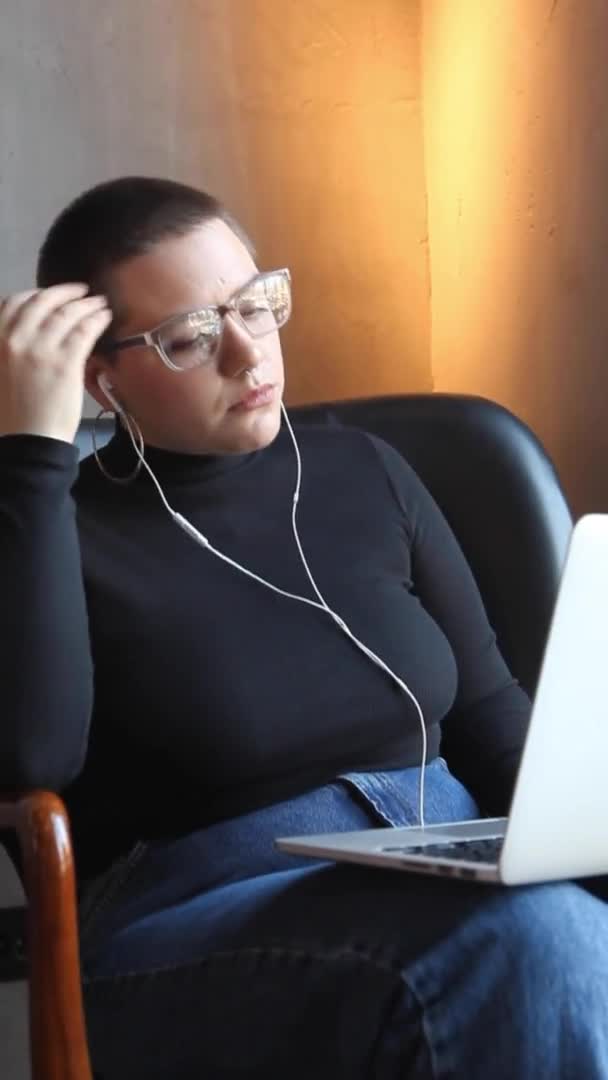 一个头戴耳机 留着短发 头戴鼻孔的小女孩正坐在咖啡店里 用笔记本电脑在视频链接上聊天 — 图库视频影像