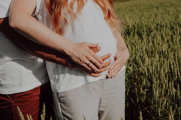 妊娠中の女性と彼女の夫と赤ちゃんのパパは 彼女の胃の上に手を保持している彼の妻を抱擁します 腕や腹部のクローズアップ — ストック写真