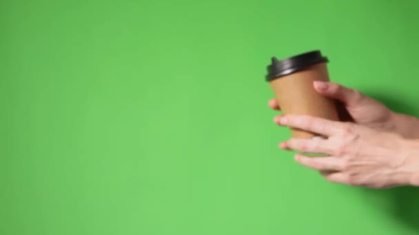手は黒の蓋で2つのカップ茶色の紙を保持 2つのコーヒー特別オファーまたはプロモーション 緑色の背景に2つのカップを保持手 紅茶やコーヒーを移動します 黒蓋の茶色い紙コップ — ストック動画