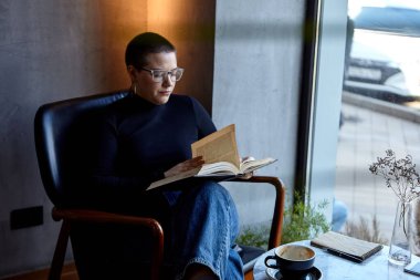 Genç bir kız bir kafede oturmuş kitap okuyor. Eğitim ve uzak çalışma kavramı 