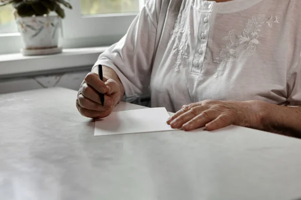 Μια Ηλικιωμένη Γυναίκα Γράφει Στο Σπίτι Ένα Κομμάτι Χαρτί Χόμπι — Φωτογραφία Αρχείου