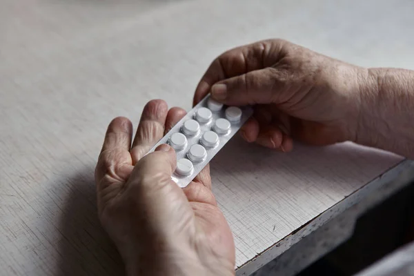 Sad old woman taking pills, health problems in old age, expensive medications. An elderly woman\'s hands unpacking several pills for taking medication. Grandma takes tablet and drinks a glass of water