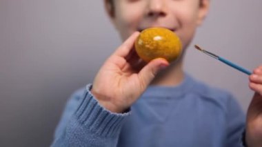 Küçük bir çocuk masaya mavi bir arka plan üzerine paskalya yumurtası çiziyor. Küçük çocuk evde boyalı Paskalya yumurtalarını boyuyor. Çocukların Paskalya yaratıcılığı. Paskalya yumurtalarını bir çocuk süslüyor..
