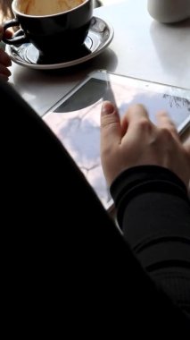 Kısa saçlı ve burun piercingli genç bir kız bir kafede oturuyor ve tablette çalışıyor. Serbest çalışma ve uzak çalışma kavramı. Bir kadın kahve içer ve grafik tabletine kalemle çizer.