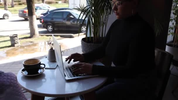 ショートヘア 鼻ピアスをした若い女の子がカフェに座ってノートパソコンで作業しています フリーランスとリモートワークやトレーニングの概念 — ストック動画