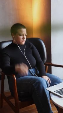 Kulaklık takan, kısa saçlı ve burun piercingli genç bir kız bir kafede oturuyor ve laptopun yanındaki video bağlantısıyla konuşuyor.