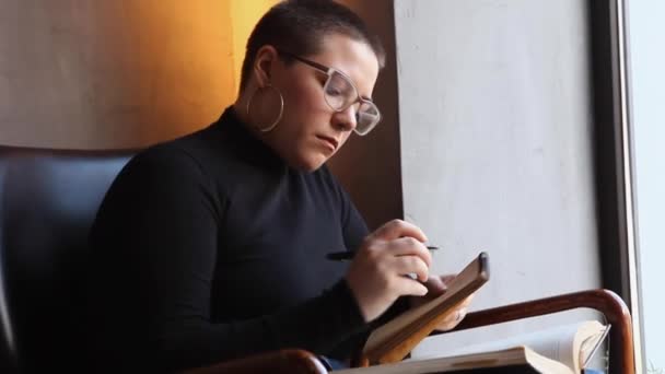 Ένα Νεαρό Κορίτσι Γυαλιά Κοντά Μαλλιά Κάθεται Ένα Καφέ Και — Αρχείο Βίντεο