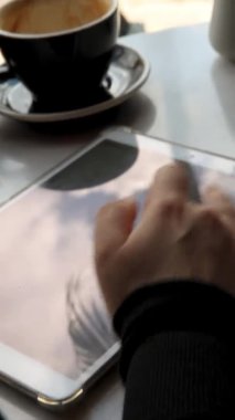 Kısa saçlı ve burun piercingli genç bir kız bir kafede oturuyor ve tablette çalışıyor. Serbest çalışma ve uzak çalışma kavramı..