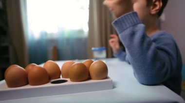 Küçük bir çocuk masaya mavi bir arka plan üzerine paskalya yumurtası çiziyor. Küçük çocuk evde boyalı Paskalya yumurtalarını boyuyor. Çocukların Paskalya yaratıcılığı. Paskalya yumurtalarını bir çocuk süslüyor..