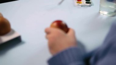 Küçük bir çocuk masaya mavi bir arka plan üzerine paskalya yumurtası çiziyor. Küçük çocuk evde boyalı Paskalya yumurtalarını boyuyor. Çocukların Paskalya yaratıcılığı. Paskalya yumurtalarını bir çocuk süslüyor..