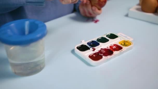 Een Klein Kind Schildert Een Paaseieren Aan Tafel Een Blauwe — Stockvideo