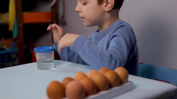 Een Klein Kind Schildert Een Paaseieren Aan Tafel Een Blauwe — Stockvideo