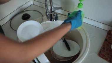 Önlüklü ve lastik eldivenli bir kadın mutfaktaki lavaboda kirli bulaşıkları yıkıyor. Bulaşık yıkamak için lavaboda kirli bulaşıklar.