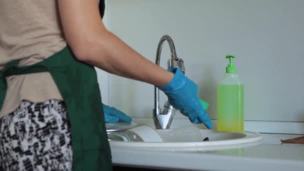 エプロンとゴム手袋の女性は台所の流しで汚れた皿を洗う 洗濯のためのシンクで汚い料理 — ストック動画
